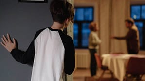 Junge beobachtet im Hintergrund streitende Eltern – Symbolik für emotionale Belastung und Erziehungsfehler