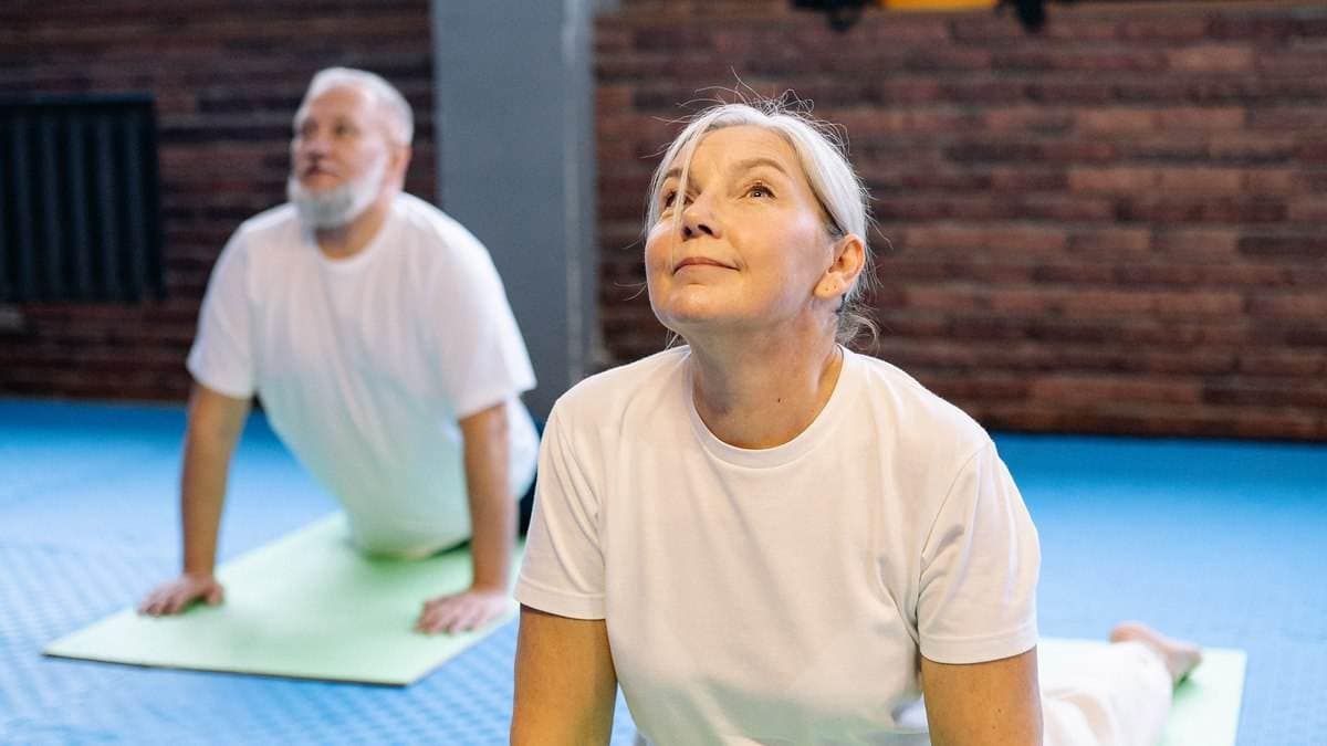 Reife Frau führt Kobra-Dehnübung auf Gymnastikmatte zur Entlastung der Bandscheibe aus