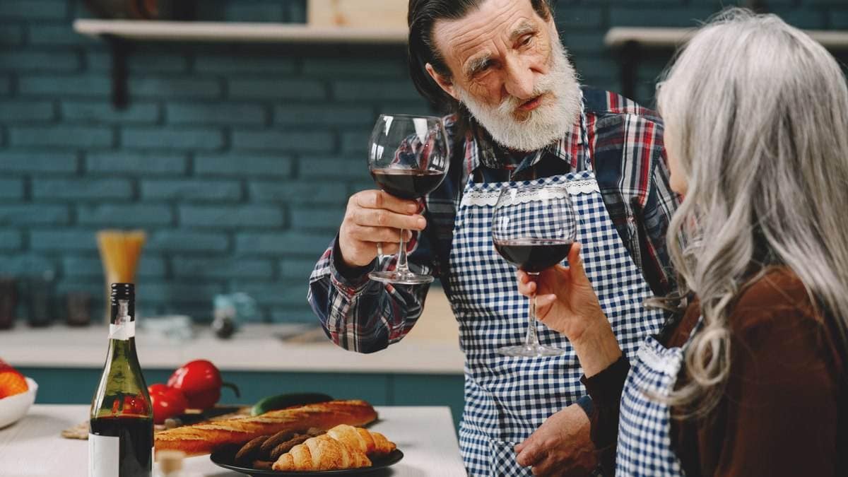 Vitales älteres Paar kocht gemeinsam und stößt mit Rotwein an – gesundes Altern mit Genuss