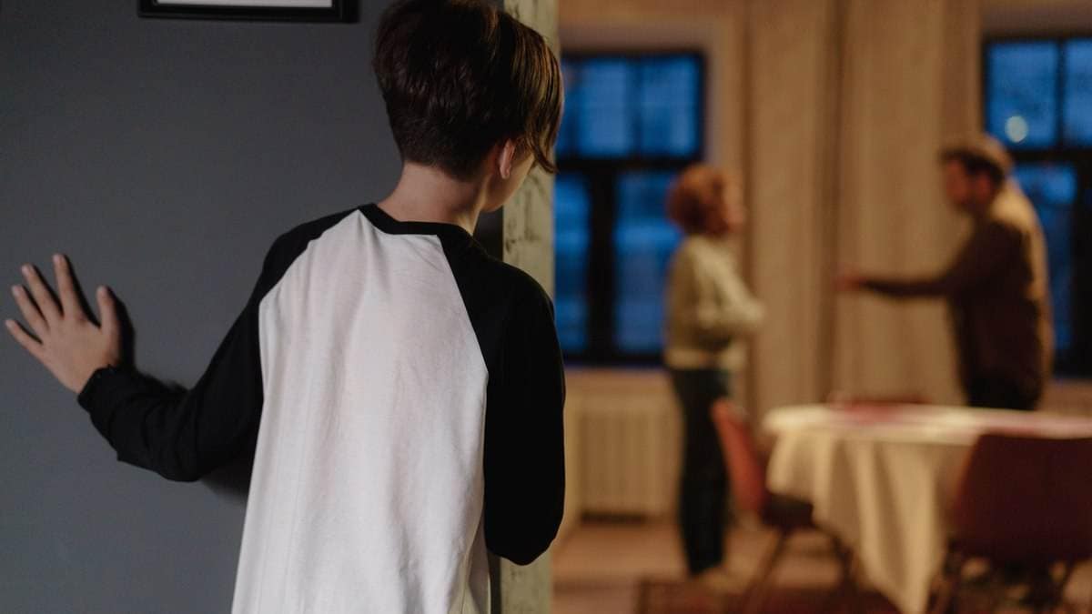 Junge beobachtet im Hintergrund streitende Eltern – Symbolik für emotionale Belastung und Erziehungsfehler