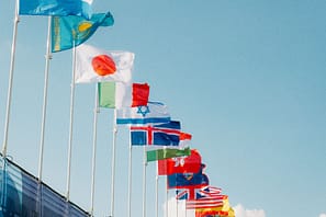 Nationalflaggen verschiedener Länder wehen nebeneinander vor blauem Himmel – Symbol für internationale Diplomatie und Frieden